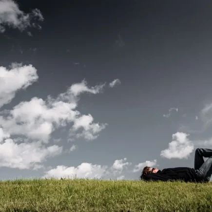 Person lying on the grass under a cloudy sky, reflecting on a peaceful Sunday routine and enjoying nature – YesvsNo.net.