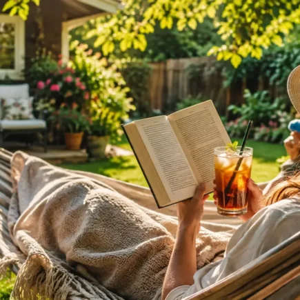 A person relaxing in a hammock or lounge chair in their own backyard with a book and iced drink, warm sunny afternoon, cozy and content mood.yes or no to taking a staycation this summer featured image.