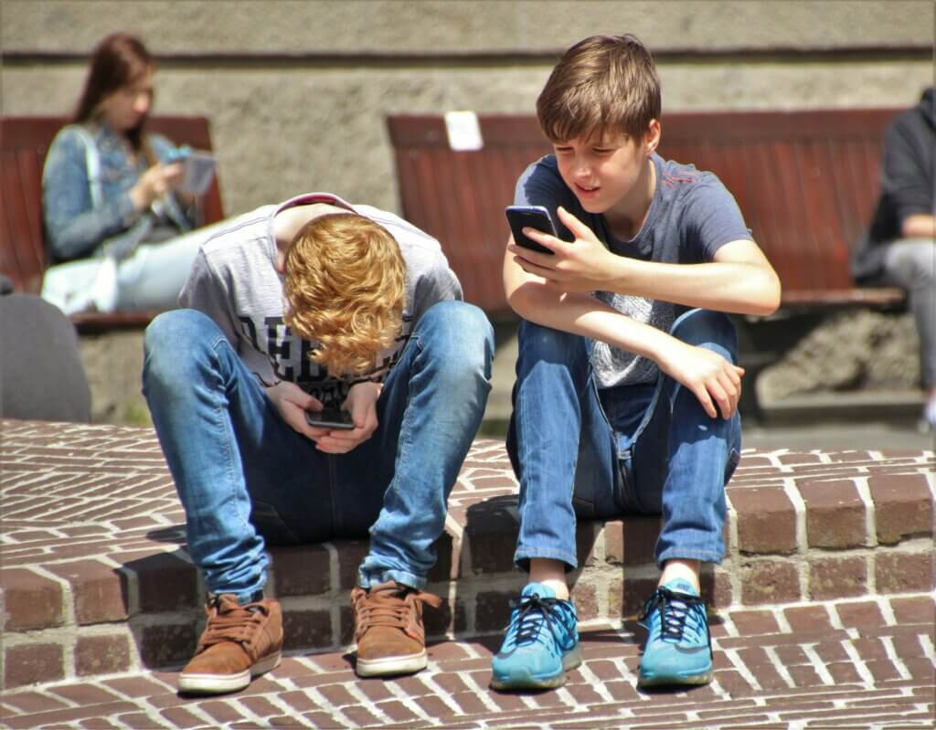 ChatGPT said:

Two boys sitting on brick steps, each focused on their smartphones. One boy leans forward, engrossed in his screen, while the other looks at his phone with a slight smile. In the background, a young woman sits on a bench, also using a phone. The scene highlights the pervasive influence of social media on daily life, raising the question, should you quit social media?