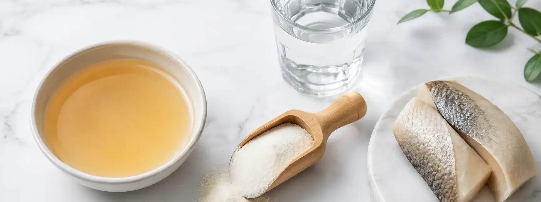 Flat lay of collagen supplement powder in a wooden scoop with a glass of water and bone broth in a bowl on a clean white marble surface, bright natural lighting, minimal editorial style — collagen supplement powder and natural sources, yes or no to collagen supplements.
