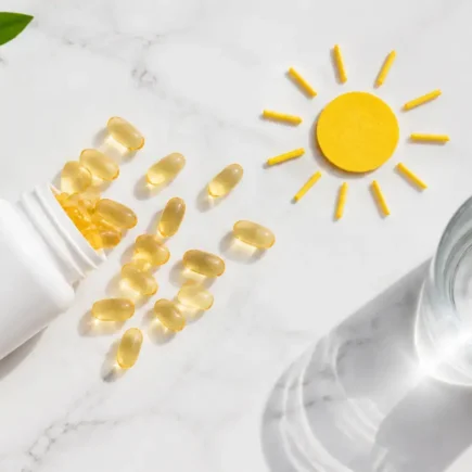 Flat lay of Vitamin D supplement capsules spilling from a white bottle onto a bright marble surface with a glass of water and a sun motif symbolizing sunlight exposure, clean minimal health concept — vitamin D supplement benefits daily use - YesVsNo.net.