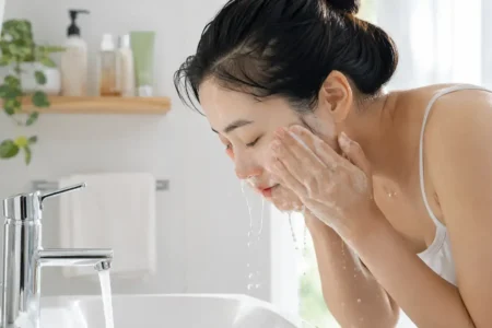 A person with bare, makeup-free skin washing their face with a simple gel cleanser at a bright bathroom sink, natural morning light, minimal product shelf visible.yes or no to double cleansing without makeup featured image.