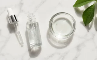 Niacinamide serum bottle with dropper and water bowl on a clean marble surface in minimal skincare style — niacinamide serum for oily skin routine - yes or no to niacinamide for oily skin.