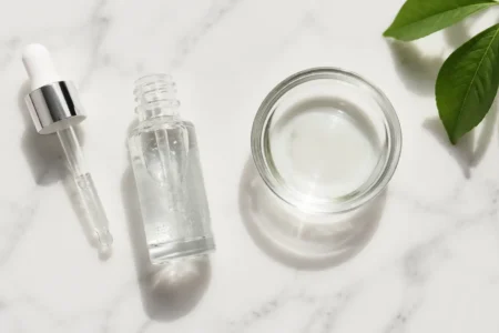 Niacinamide serum bottle with dropper and water bowl on a clean marble surface in minimal skincare style — niacinamide serum for oily skin routine - yes or no to niacinamide for oily skin.