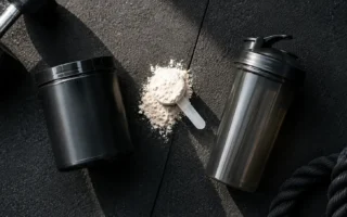 Top-down flat lay of a pre-workout supplement tub, a scoop of powder, and a shaker bottle on a dark gym floor under natural light — pre-workout supplement powder and shaker bottle - yes or no to pre-workout for fat loss.