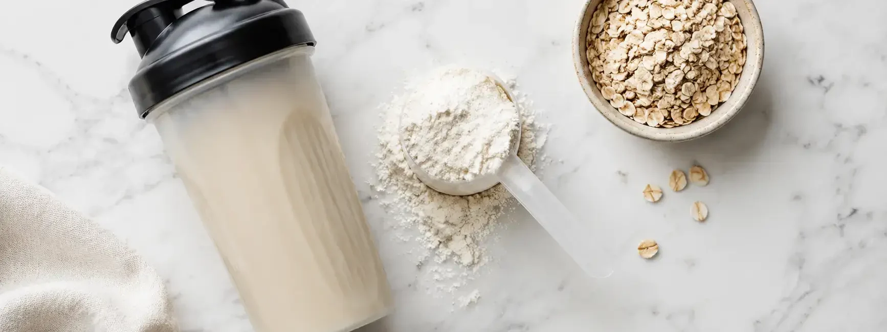 Protein shake powder with a shaker bottle and oats on a clean marble surface under bright natural light — protein shake powder and whole food protein sources - yes or no to protein shakes daily.