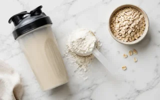 Protein shake powder with a shaker bottle and oats on a clean marble surface under bright natural light — protein shake powder and whole food protein sources - yes or no to protein shakes daily.