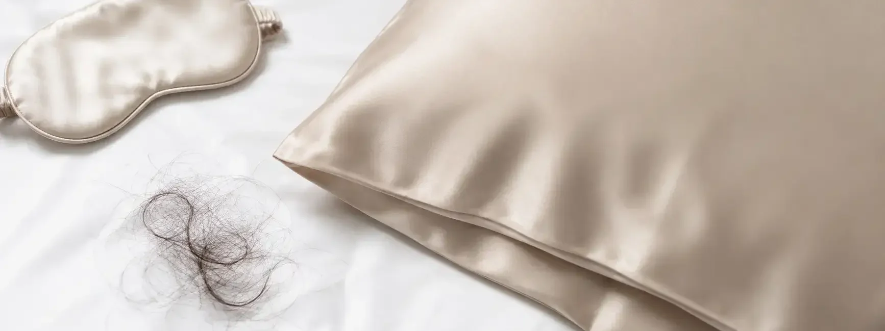 A flat lay of a silk pillowcase in a soft neutral color, a few strands of hair beside it, and a small satin sleep mask on a clean white surface. Soft natural lighting, minimal style. No text overlays.yes or no to silk pillowcases for hair fall