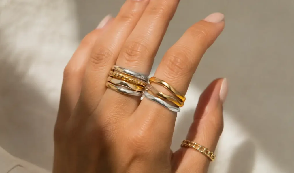 Close-up of a hand wearing a mix of gold and silver rings stacked together, neutral background, soft natural light highlighting the metal contrast-yes or no to mixing gold and silver jewelry featured image.