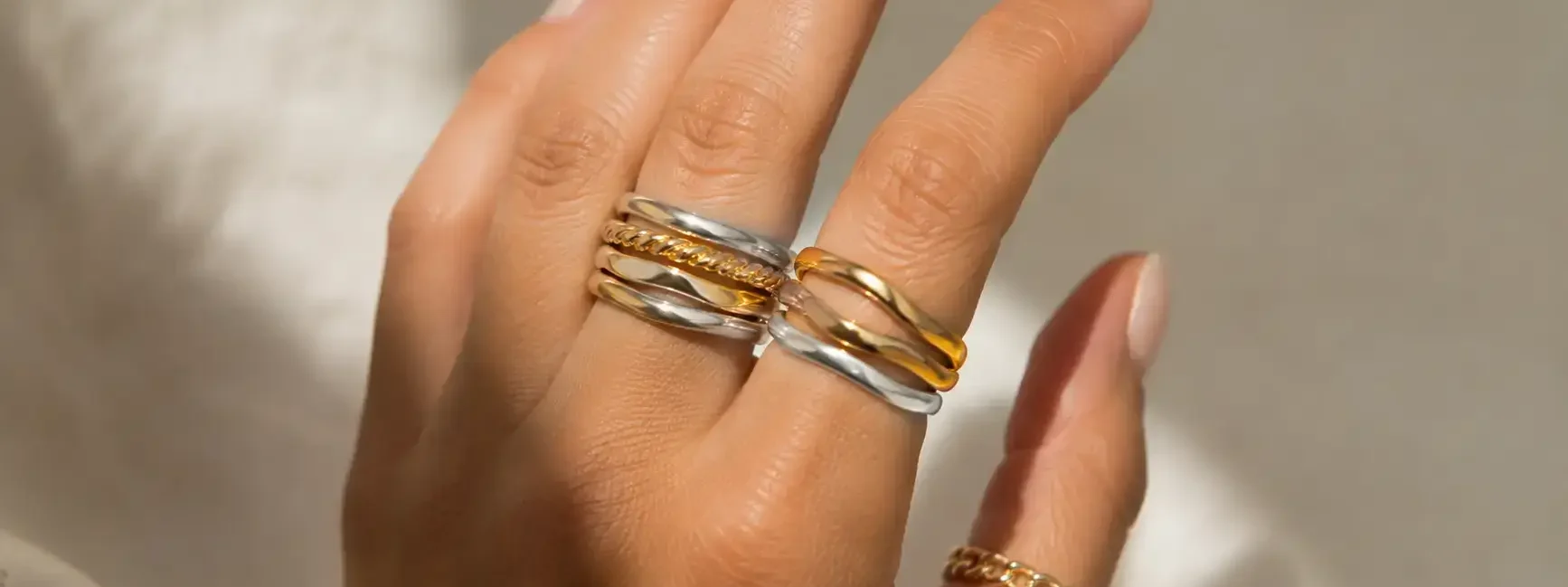 Close-up of a hand wearing a mix of gold and silver rings stacked together, neutral background, soft natural light highlighting the metal contrast-yes or no to mixing gold and silver jewelry featured image.