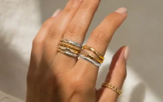 Close-up of a hand wearing a mix of gold and silver rings stacked together, neutral background, soft natural light highlighting the metal contrast-yes or no to mixing gold and silver jewelry featured image.