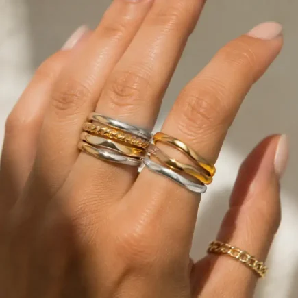 Close-up of a hand wearing a mix of gold and silver rings stacked together, neutral background, soft natural light highlighting the metal contrast-yes or no to mixing gold and silver jewelry featured image.