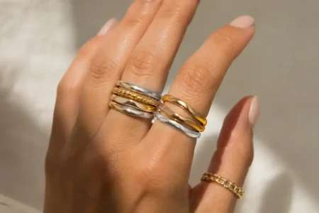 Close-up of a hand wearing a mix of gold and silver rings stacked together, neutral background, soft natural light highlighting the metal contrast-yes or no to mixing gold and silver jewelry featured image.